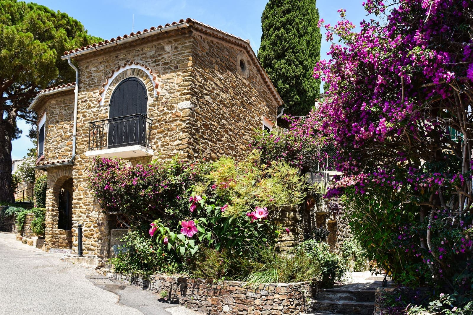 Una casa de piedra con una ventana en arco, rodeada de buganvillas y cipreses