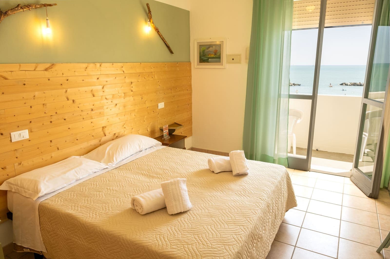 Una habitación de hostal con cama de matrimonio, toallas dobladas y la puerta del balcón abierta al mar
